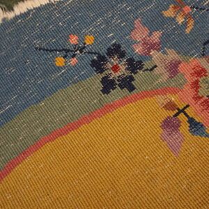 Detailed view of a flat, ribbed weave rug showing segmented blue, green, and gold fields with floral designs.