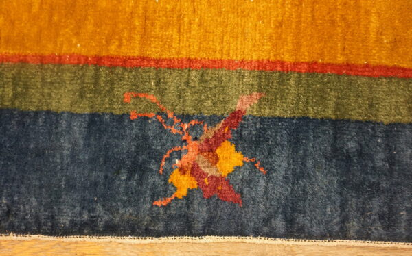 Abstract rug detail showing bands of gold, red, green, and navy with a stylized central pattern.