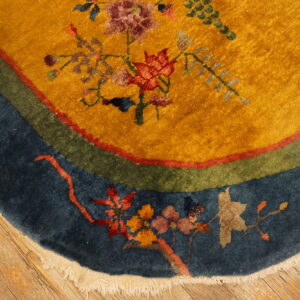 Mustard-yellow rug with floral design and blue, green, and red borders rests on wood floors.