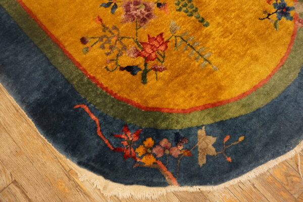 Mustard-yellow rug with floral design and blue, green, and red borders rests on wood floors.
