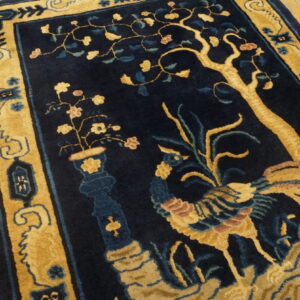 High-contrast navy and gold rug featuring a stylized bird, tree, and vase pattern on wood flooring.