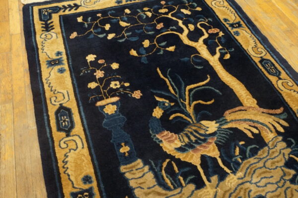 High-contrast navy and gold rug featuring a stylized bird, tree, and vase pattern on wood flooring.