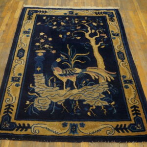Low-pile, dark blue rug featuring a gold pictorial tree and bird pattern rests on hardwood flooring.