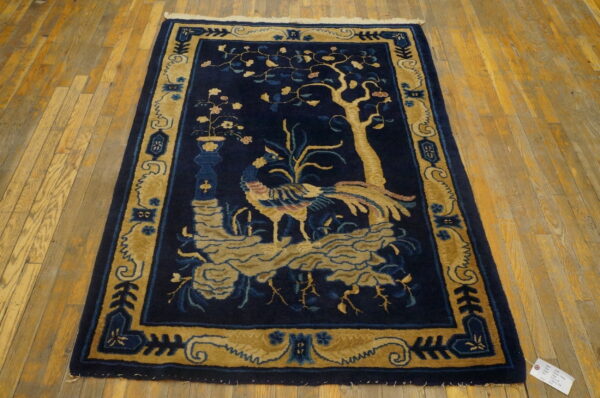 Low-pile, dark blue rug featuring a gold pictorial tree and bird pattern rests on hardwood flooring.