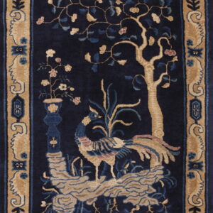 Dark blue rug with a tan border and central design featuring a tree, phoenix, and vase of flowers.