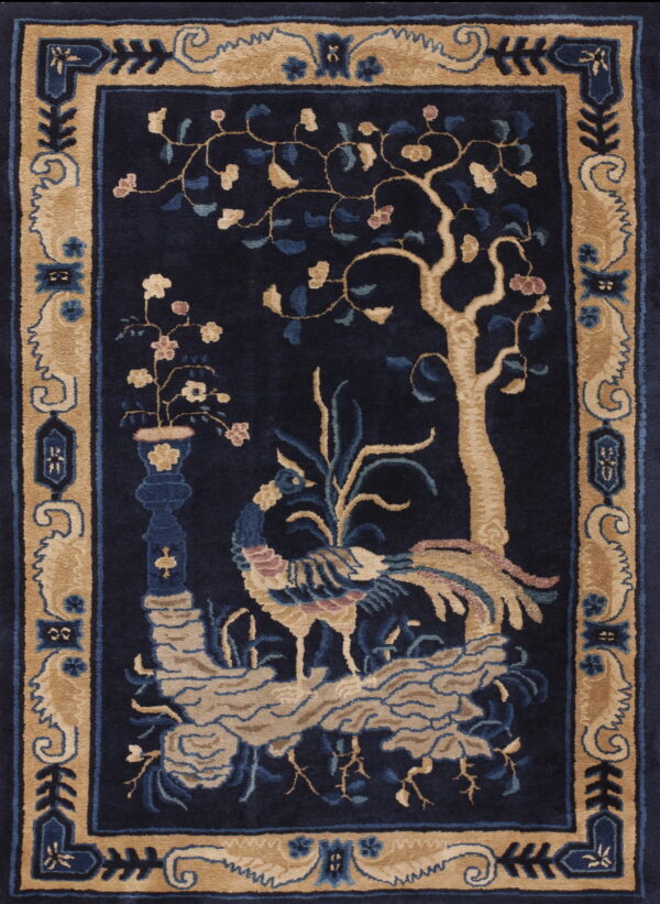 Dark blue rug with a tan border and central design featuring a tree, phoenix, and vase of flowers.