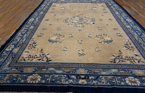 Tan field rug with detailed blue, beige, and navy borders, featuring circular floral motifs on wood flooring.