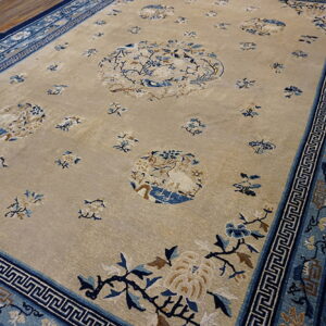 Light beige rug featuring scattered blue floral medallions and a broad multi-layered blue patterned border on wood flooring.
