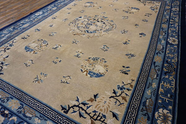 Light beige rug featuring scattered blue floral medallions and a broad multi-layered blue patterned border on wood flooring.