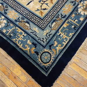 Ornate navy and powder blue rug with floral and geometric borders lies on distressed wood planks.