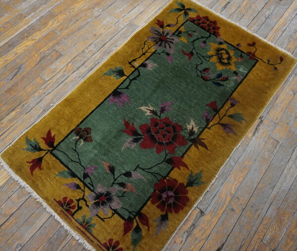 Gold-bordered rug featuring a teal center with red, purple, and yellow floral patterns on distressed wood planks.