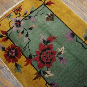 Low-pile rug with a sage green center, golden border, and large red floral pattern on distressed wood planks.