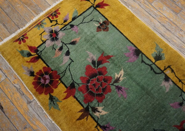 Low-pile rug with a sage green center, golden border, and large red floral pattern on distressed wood planks.