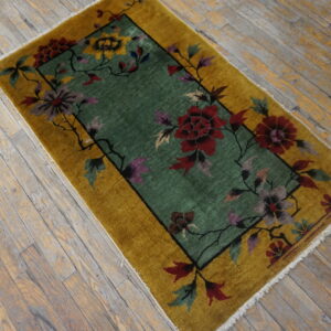 Gold border rug with a green field and multi-colored floral pattern on worn wooden floors.