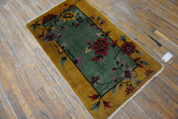 Gold border rug with a green field and multi-colored floral pattern on worn wooden floors.