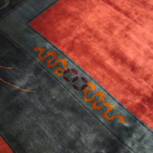 Dark teal rug border with orange vines and purple motifs meets a vibrant reddish-pink field.