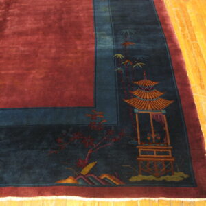 Velvety red rug with a blue border depicting a pagoda and flowers rests on yellow wood flooring.