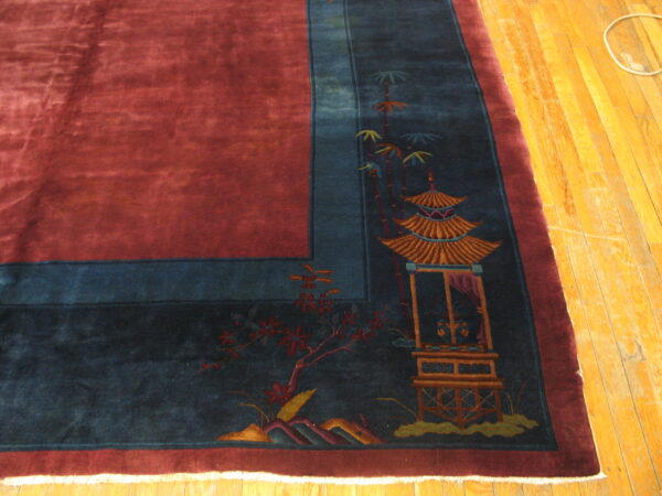 Velvety red rug with a blue border depicting a pagoda and flowers rests on yellow wood flooring.