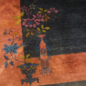 Dark navy rug with rust border featuring blue and pink floral vase motifs on wood flooring.