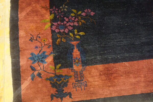 Dark navy rug with rust border featuring blue and pink floral vase motifs on wood flooring.