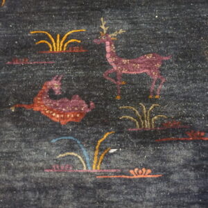 Dark blue medium-pile rug detail showing stylized magenta deer and colorful grass and plant designs.