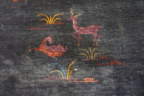 Dark blue medium-pile rug detail showing stylized magenta deer and colorful grass and plant designs.