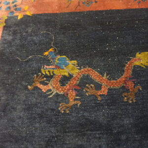 Dark navy rug with a sparkling red dragon design adjacent to a floral terracotta border.