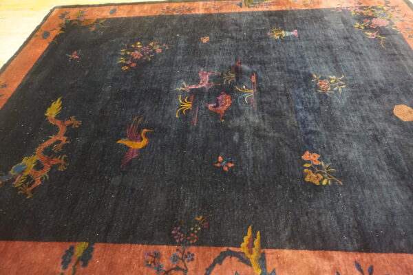 Low pile navy rug with scattered colorful patterns of dragons, birds, and flowers, framed by a rust-colored border.
