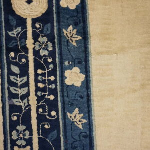 High pile rug features a cream field next to a dark blue border panel with stylized floral designs.