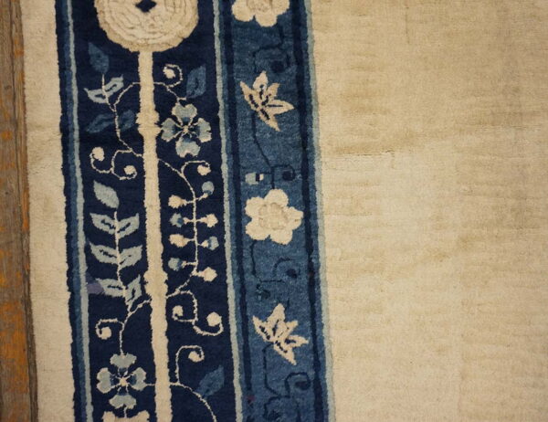 High pile rug features a cream field next to a dark blue border panel with stylized floral designs.