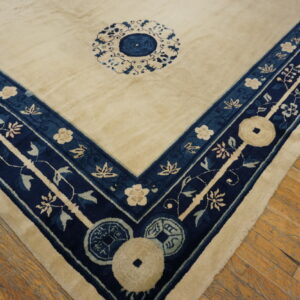 A cream field rug with a detailed navy blue and ivory floral border sits on hardwood planks.