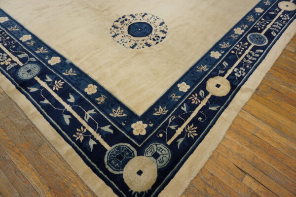 A cream field rug with a detailed navy blue and ivory floral border sits on hardwood planks.