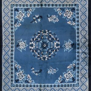 A blue square rug with cream and navy floral patterns rests on wide plank wood flooring.