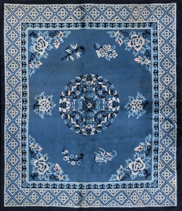 A blue square rug with cream and navy floral patterns rests on wide plank wood flooring.