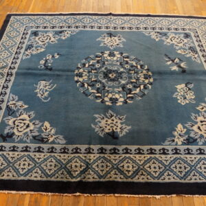 Teal rug with cream and navy floral patterns and geometric borders sits on polished hardwood floors.