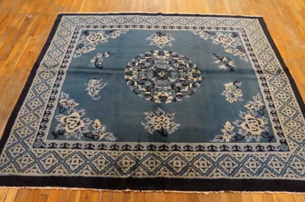 Teal rug with cream and navy floral patterns and geometric borders sits on polished hardwood floors.
