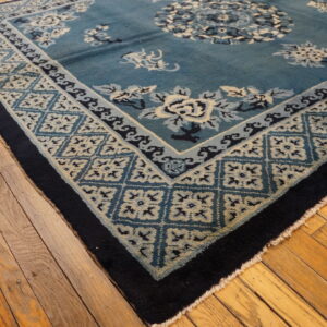 Teal and navy blue rug featuring cream floral patterns and geometric borders sits on distressed wooden flooring.