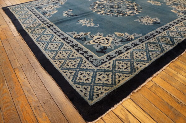 Teal and navy blue rug featuring cream floral patterns and geometric borders sits on distressed wooden flooring.