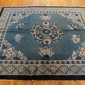 Teal floral rug with cream, light blue, and navy details displayed on warm wooden plank flooring.