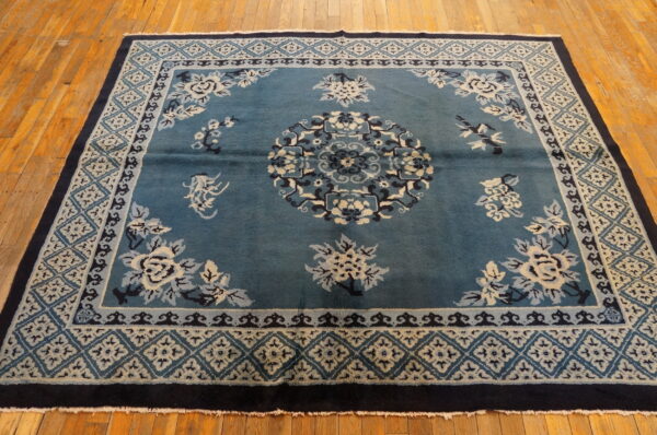 Teal floral rug with cream, light blue, and navy details displayed on warm wooden plank flooring.