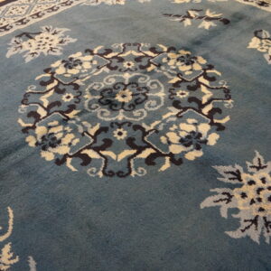 Dusty blue rug with a navy and cream floral pattern rests against light wood flooring.