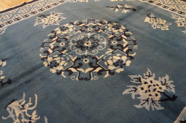 Dusty blue rug with a navy and cream floral pattern rests against light wood flooring.
