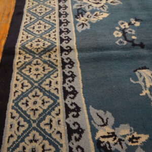 Teal rug with contrasting beige and navy floral and geometric patterns sits on worn wood planks.