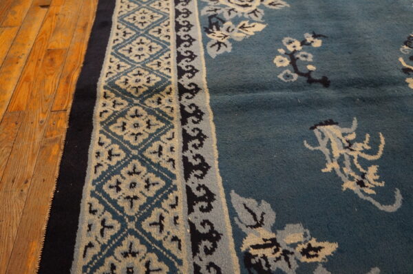 Teal rug with contrasting beige and navy floral and geometric patterns sits on worn wood planks.