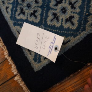 Textured blue rug with geometric pattern and dark border rests on a glossy wood floor.