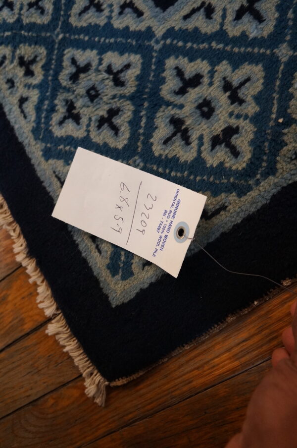 Textured blue rug with geometric pattern and dark border rests on a glossy wood floor.