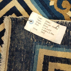 A blue, tan, and gold rug displaying geometric and scroll patterns with a large white product label attached.