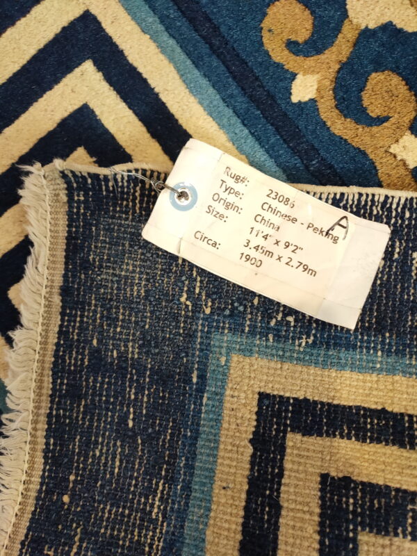 A blue, tan, and gold rug displaying geometric and scroll patterns with a large white product label attached.