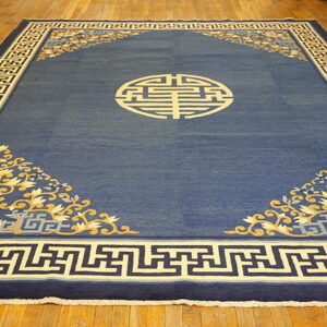 A deep blue rug features a central beige geometric medallion, floral corner designs, and a key pattern border.