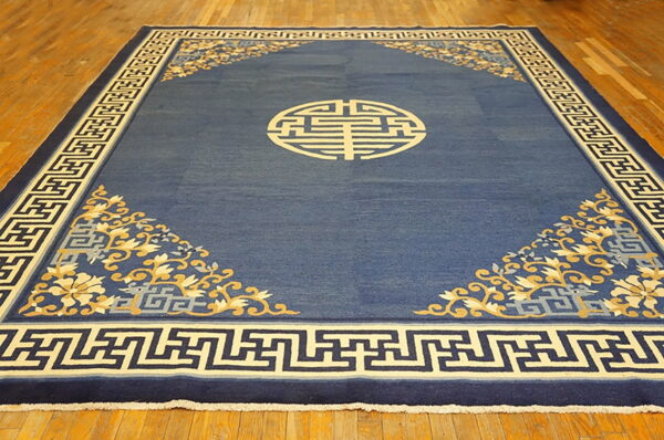 A deep blue rug features a central beige geometric medallion, floral corner designs, and a key pattern border.